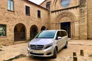 Taxi monovolumen Mercedes estacionado frente a un monasterio románico durante un trayecto de largo recorrido desde el Vallès Oriental