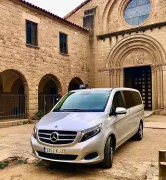Taxi monovolumen Mercedes estacionado frente a un monasterio románico durante un trayecto de largo recorrido desde el Vallès Oriental