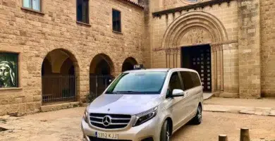 Taxi monovolumen Mercedes estacionado frente a un monasterio románico durante un trayecto de largo recorrido desde el Vallès Oriental