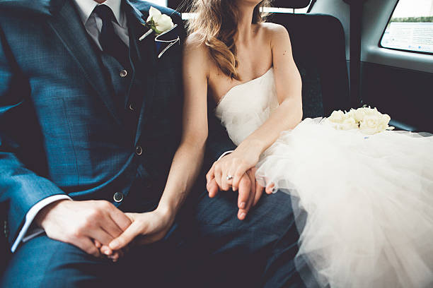 Pareja de novios cogidos de la mano en el asiento trasero de un taxi el día de su boda con el ramo de flores blancas
